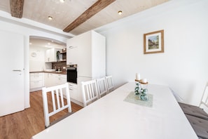 Cozinha moderna com armários brancos, uma mesa de jantar com cadeiras brancas e um quadro pendurado na parede.