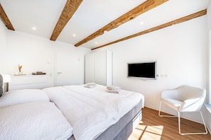 Quarto moderno com cama grande, TV na parede e uma cadeira.