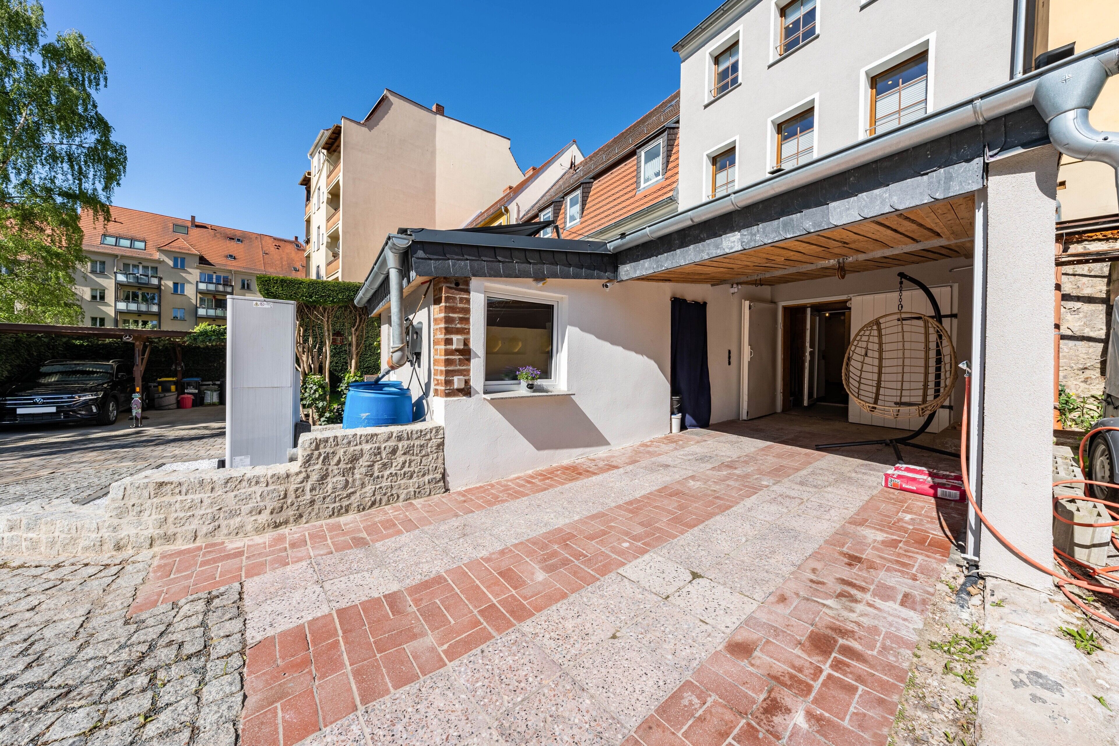Ein Wohngebäude mit Pflasterterrasse, Hängesessel und sichtbarer Garage.