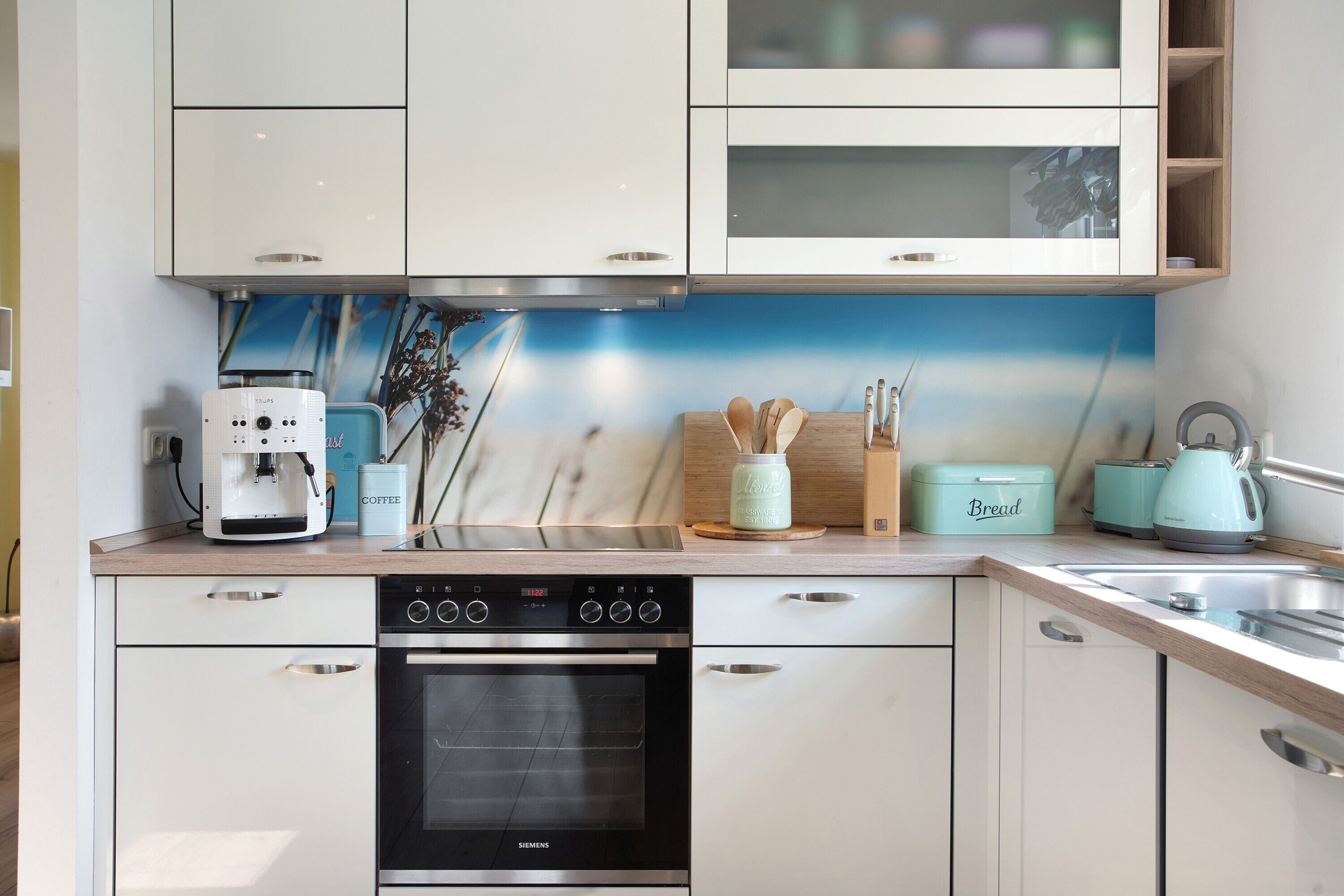 Une cuisine moderne avec des meubles blancs, un four Siemens, une machine à café et un grille-pain.