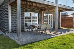 A patio area with a brick exterior, a wooden table with chairs, and a covered seating area. - Apartment 'Komfortables Ferienhaus Allee' with Private Terrace, Private Garden and Wi-Fi (Krummin)