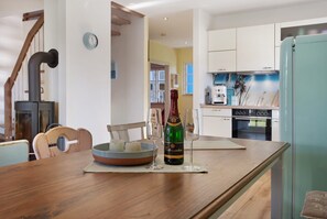 Une cuisine avec une table en bois, une bouteille de champagne et un saladier de fruits.