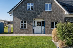 A two-story brick house with a white door, a small porch, and a solar panel on the roof. - Apartment 'Komfortables Ferienhaus Allee' with Private Terrace, Private Garden and Wi-Fi (Krummin)