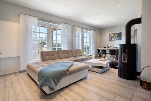 A modern living room with a sectional sofa, a coffee table, a fireplace, and large windows. - Apartment 'Komfortables Ferienhaus Hafen' with Private Terrace, Private Garden and Wi-Fi (Krummin)