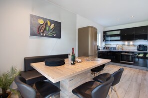 A modern kitchen with a built-in oven, a large refrigerator, and a dining area with a wooden table and black chairs. - Apartment 'Komfortables Ferienhaus Hafen' with Private Terrace, Private Garden and Wi-Fi (Krummin)