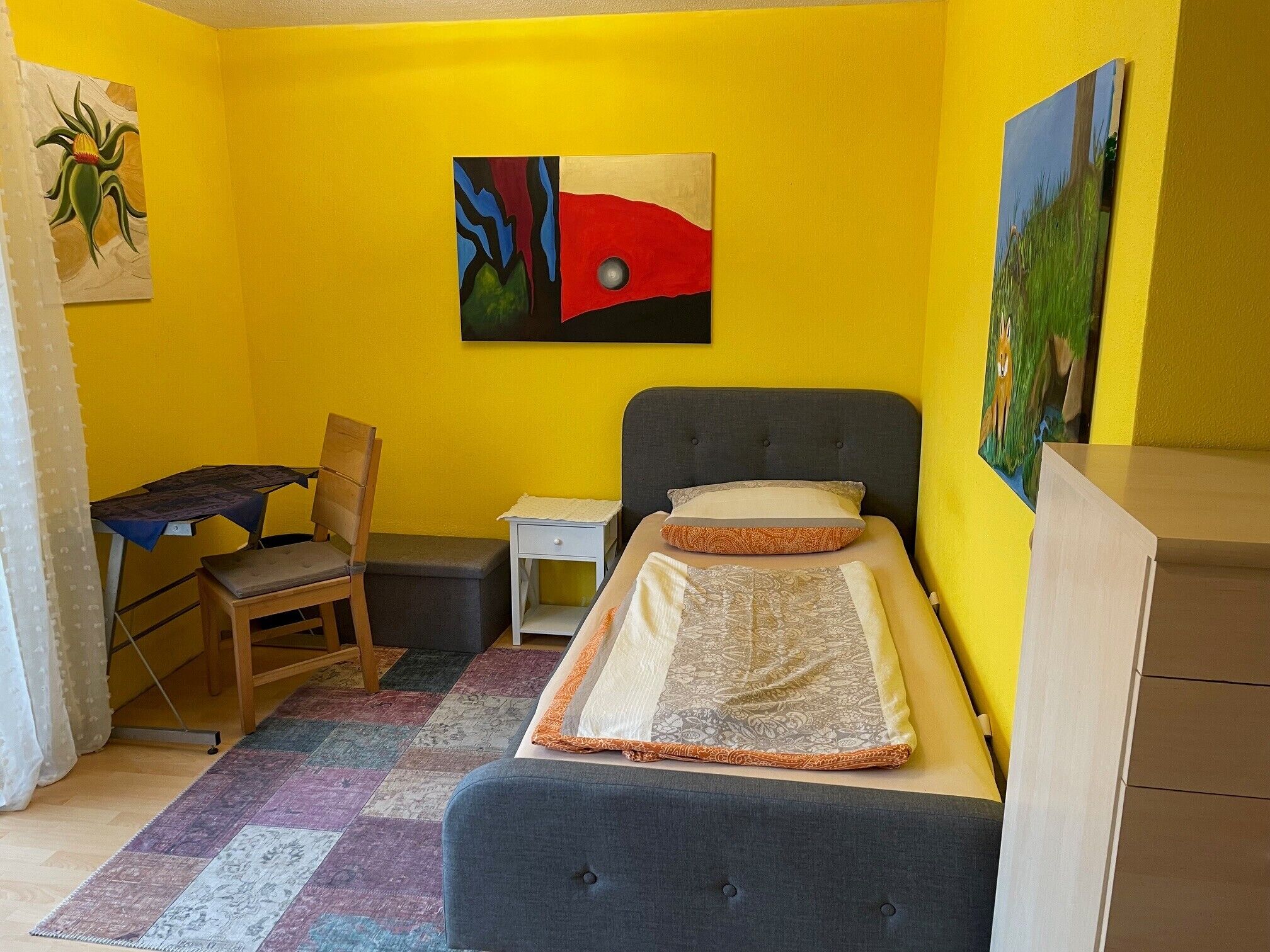 Een kleine, kleurrijke kamer met een bed, bureau en stoel.
