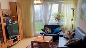 A living room with a sofa, a TV, a table with a candle, and a bed. - Holiday Apartment Ingrid Rautenberg with Private Terrace, Garden and Wi-Fi (Krautheim)