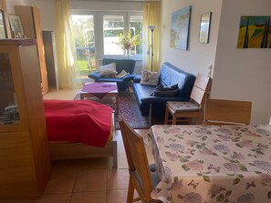 Une pièce comprenant un lit, un canapé, une table et une chaise. Il y a une fenêtre avec des rideaux, une lampe et des œuvres d’art accrochées au mur.