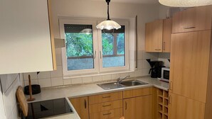 A kitchen with a window, wooden cabinets, a sink, and a stove. - Holiday Apartment Ingrid Rautenberg with Private Terrace, Garden and Wi-Fi (Krautheim)