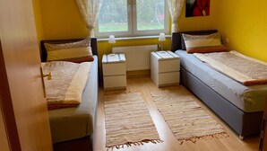 A room with two beds, a window with curtains, a radiator, and a painting on the wall. - Holiday Apartment Ingrid Rautenberg with Private Terrace, Garden and Wi-Fi (Krautheim)