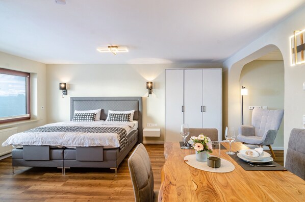 A modern bedroom with a bed, bedside tables, a dining table, and a view of the outdoors.