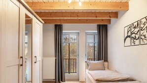 Un dormitorio con cama, ventana, radiador y puerta que da a otra habitación.