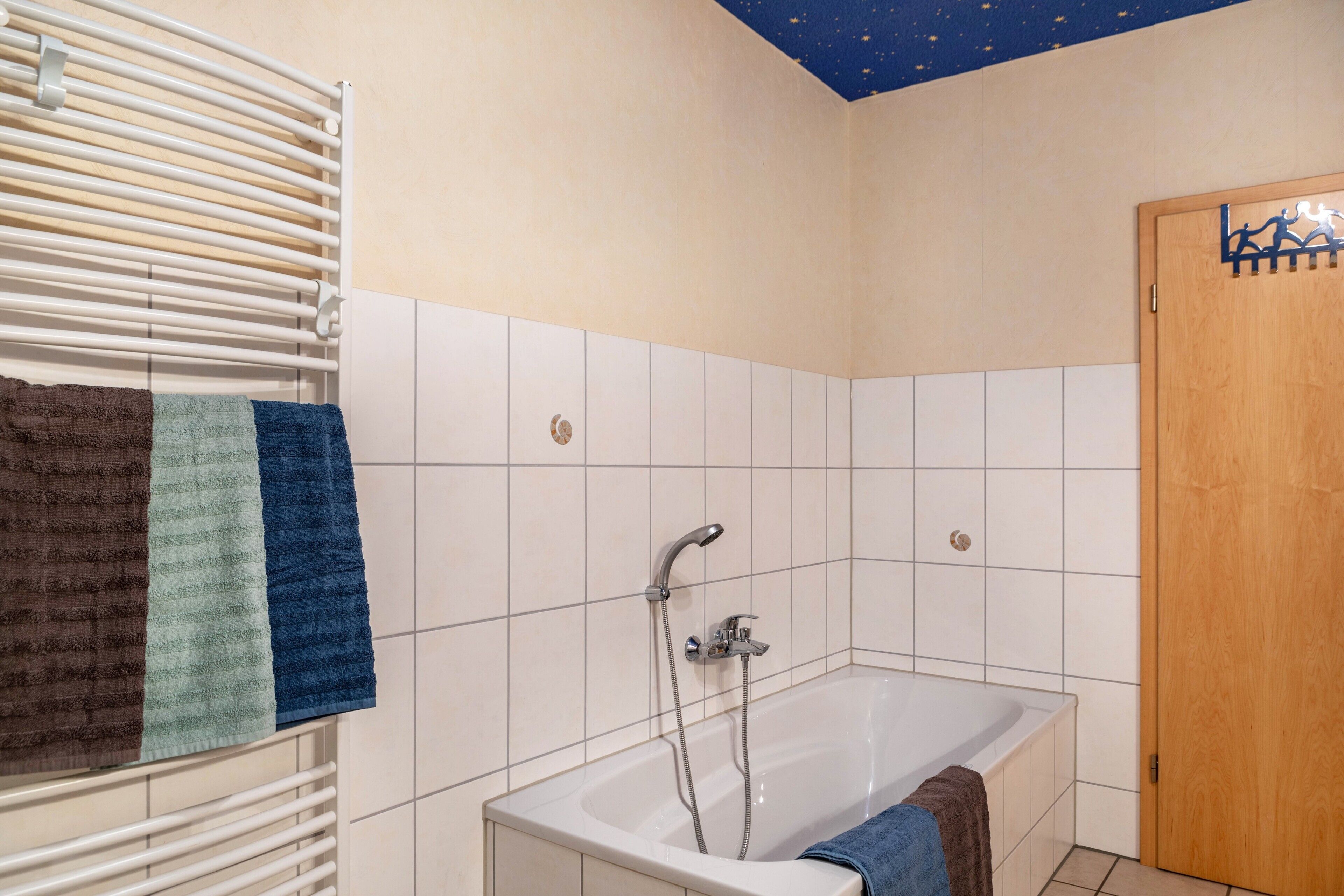 Un bagno con una vasca, un portasciugamani con asciugamani, un soffione e una porta in legno.