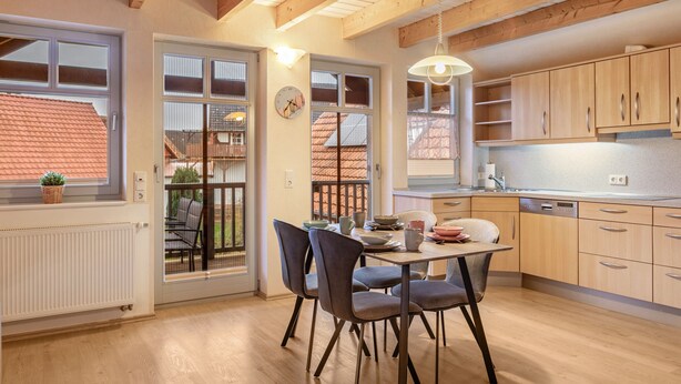 Una cocina moderna con armarios de madera, una mesa de comedor con sillas y un reloj visible en la pared.
