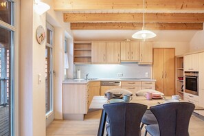 Eine moderne Küche mit Holzschränken, einem Esstisch mit Stühlen und einer Pendelleuchte.