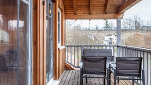 Un balcón de madera con dos sillas y una mesa, con vista a un puente y edificios.