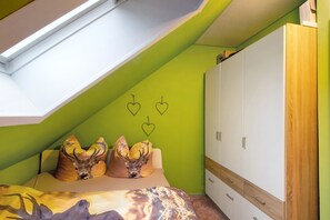 Une chambre avec un plafond en pente, un lit doté d’une tête de lit sur le thème des cerfs, une armoire et des décorations murales en forme de cœur.