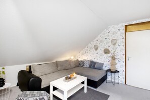 Un salon moderne avec un canapé gris, une table basse blanche et une petite table d’appoint sur laquelle est posé un vase.