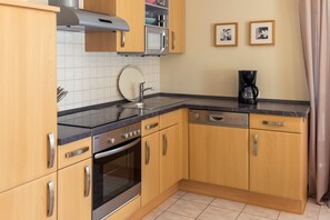 A kitchen with wooden cabinets, a stainless steel range hood, a microwave, a coffee maker, and a dishwasher.