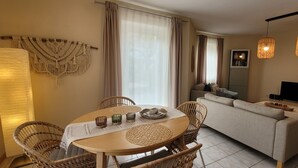 Una sala de estar moderna con sofá, mesa de comedor, sillas de mimbre, televisor de pantalla plana y lámparas colgantes.