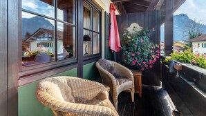 Een balkon met rieten stoelen, een houten tafel en een potplant met roze bloemen.