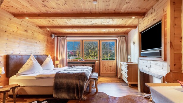 Een slaapkamer in een houten chalet met een bed, een houten dressoir, een televisie en een groot raam.
