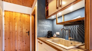 Een houten deur, een keuken met een spoelbak, kasten en een prikbord met een boodschap.