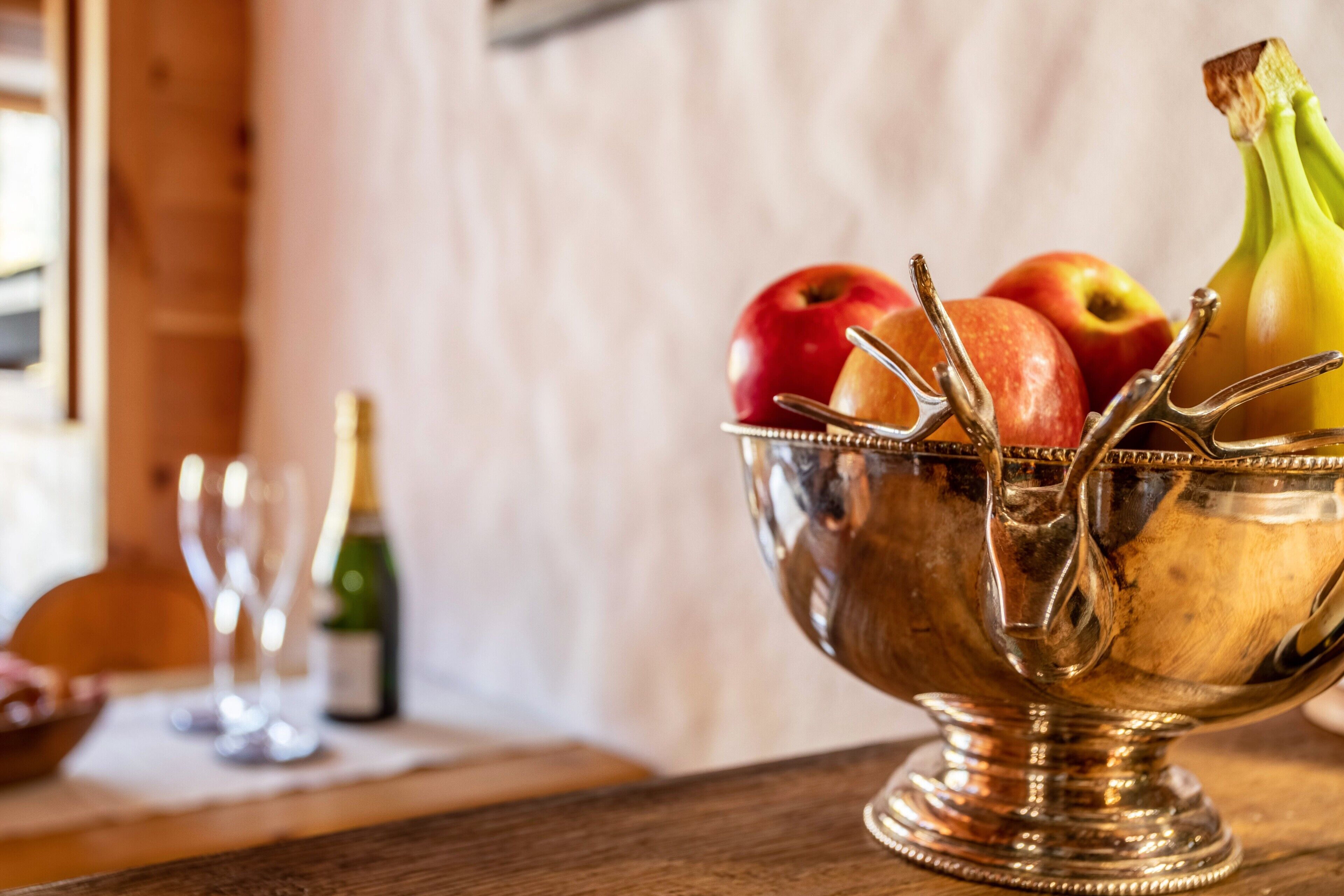 A silver bowl with fruits and a bottle on a wooden table.