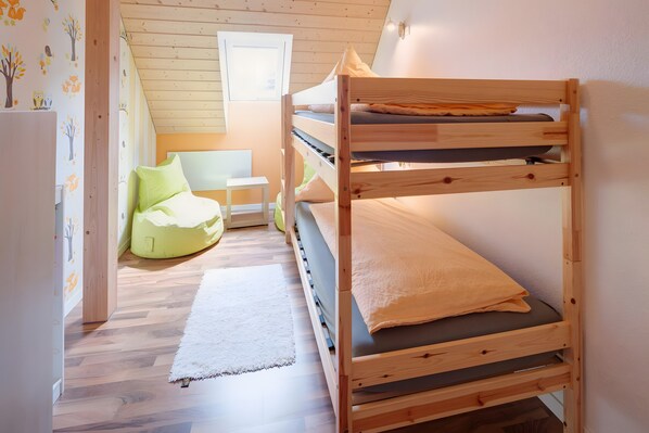 Dormitorio con literas, suelo de madera, una mesita pequeña, un sillón de peluche y una ventana.