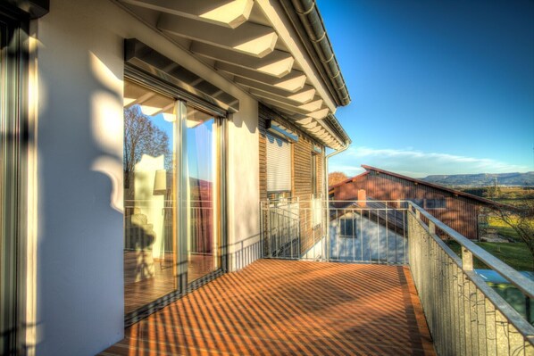 A balcony with a view of a rural landscape, a wooden deck, and a metal railing.