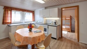 A modern kitchen with white cabinets, a dining table with a floral centerpiece, and a view of a bunk bed through an open door. - Apartment 'Glockenblume' with Shared Terrace, Shared Garden and Wi-Fi (Gerabronn)