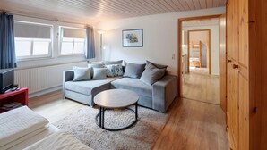 A modern living room with a grey sofa, a round coffee table, a TV on a red stand, and a wooden wardrobe. - Apartment 'Glockenblume' with Shared Terrace, Shared Garden and Wi-Fi (Gerabronn)