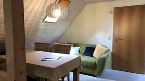 A room with a dining table, wicker chairs, a green sofa, a wooden door, and a sloped ceiling with a skylight. - Apartment 'Gänseblümchen' with Shared Terrace, Shared Garden and Wi-Fi (Gerabronn)