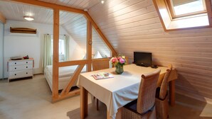 A room with a sloped ceiling, wooden beams, a bed, a desk with a computer, a dining table, wicker chairs, and a window. - Apartment 'Gänseblümchen' with Shared Terrace, Shared Garden and Wi-Fi (Gerabronn)