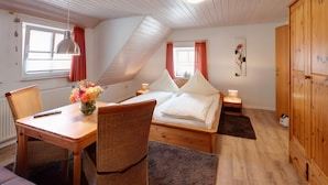 Une pièce chaleureuse comprenant un lit, une table à manger, des chaises en osier, un vase de fleurs et une armoire en bois.