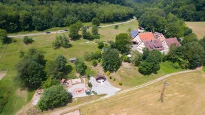 Vue aérienne d’une propriété rurale comprenant une grande maison, une petite grange et un espace de jeux clôturé.