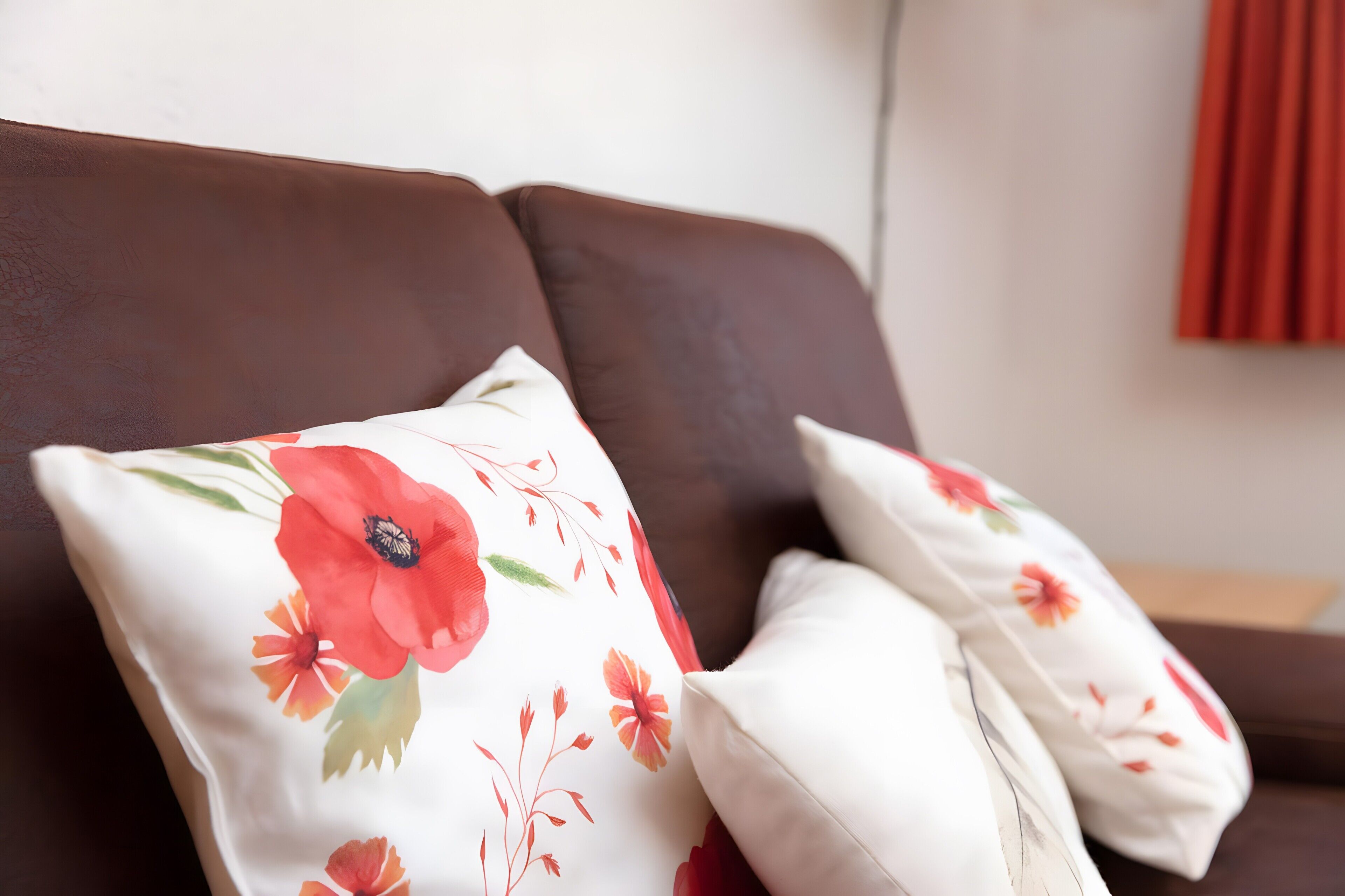 En brun soffa med två vita kuddar med röda blommönster.
