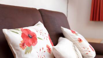 Un sofá marrón con dos almohadas blancas de estampado floral rojo.