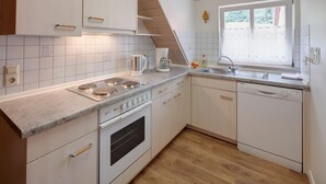 Une cuisine avec des meubles blancs, une cuisinière, un four, un lave-vaisselle et une fenêtre donnant sur un paysage verdoyant.