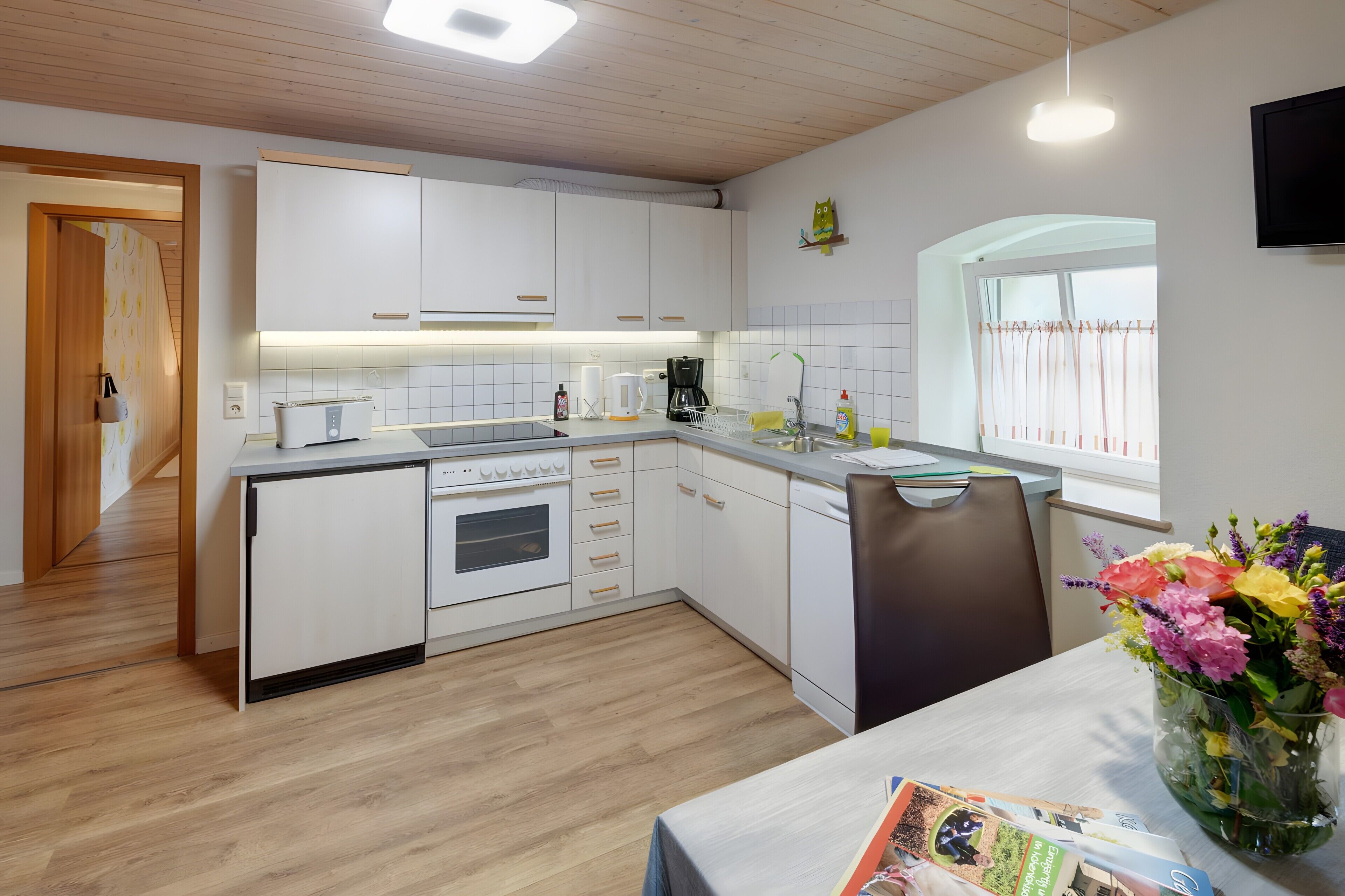 A modern kitchen with white cabinets, a built-in oven, and a dining area with a table and chairs.