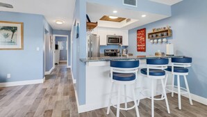 A modern kitchen with a central island, bar stools, and a microwave. - Beautifully Remodeled Waterfront Condo | Community Pool & Beach Gear | Walk to Santini Plaza & Beach (Fort Myers Beach)