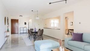 Una sala moderna con un sofá, un comedor con sillas y una mesa, y una cocina al fondo.