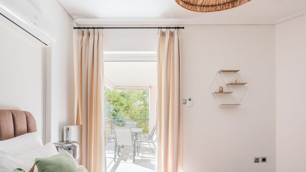 Un dormitorio con cama, mesita de noche, lámpara, ventana con cortinas, balcón con mesa y sillas, y estante montado en la pared.
