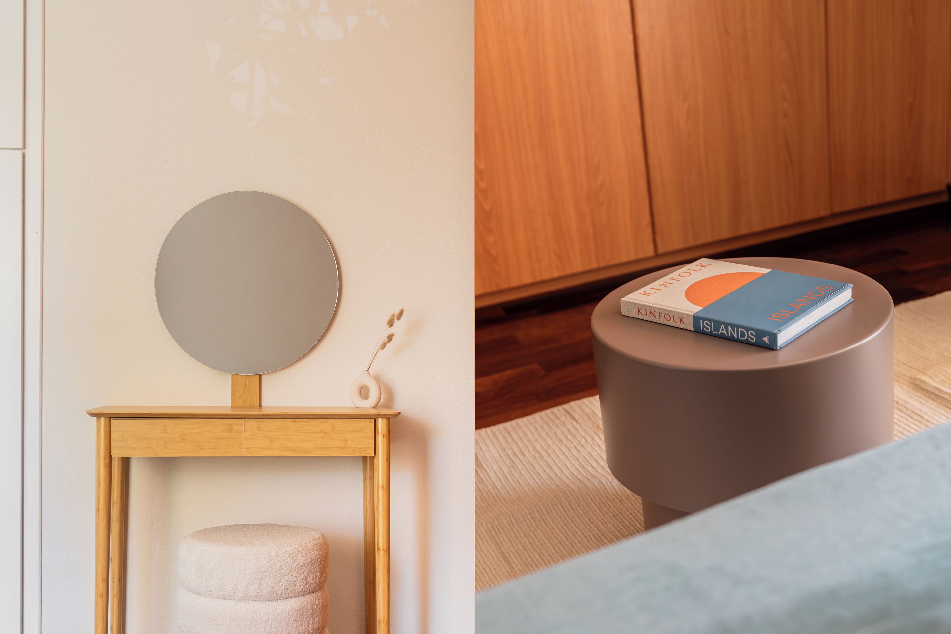 A room with a wooden bedside table, a round mirror, a small stool, and a book titled 'Kinfolk Islands'.
