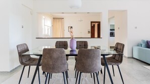 Un comedor moderno con una mesa de vidrio y seis sillas, un jarrón con plantas secas y una lámpara colgante.