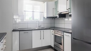 Una cocina moderna con armarios blancos, electrodomésticos de acero inoxidable y un ventanal que proporciona luz natural.