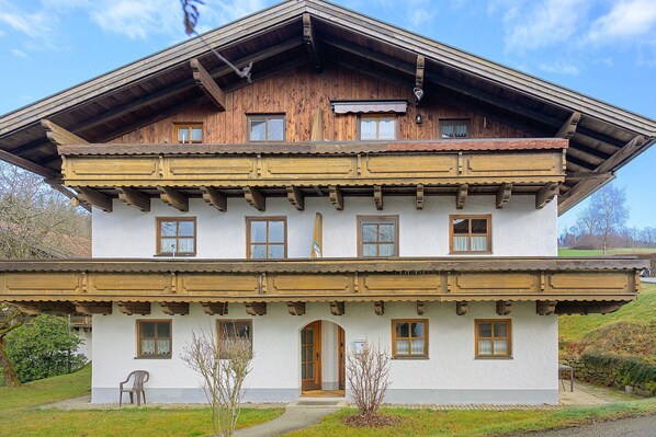 A two-story wooden house with a balcony, a front door, and a small porch area.