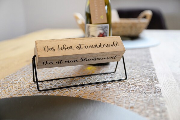 Un letrero de madera con texto sobre una mesa, un mantel tejido y un fondo desenfocado con una cesta de mimbre.