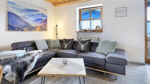 A living room with a sectional sofa, a coffee table, a painting, a window, and a sign on the wall.