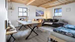 A cozy room with a wooden ceiling, a dining table, a sofa, and a bed.